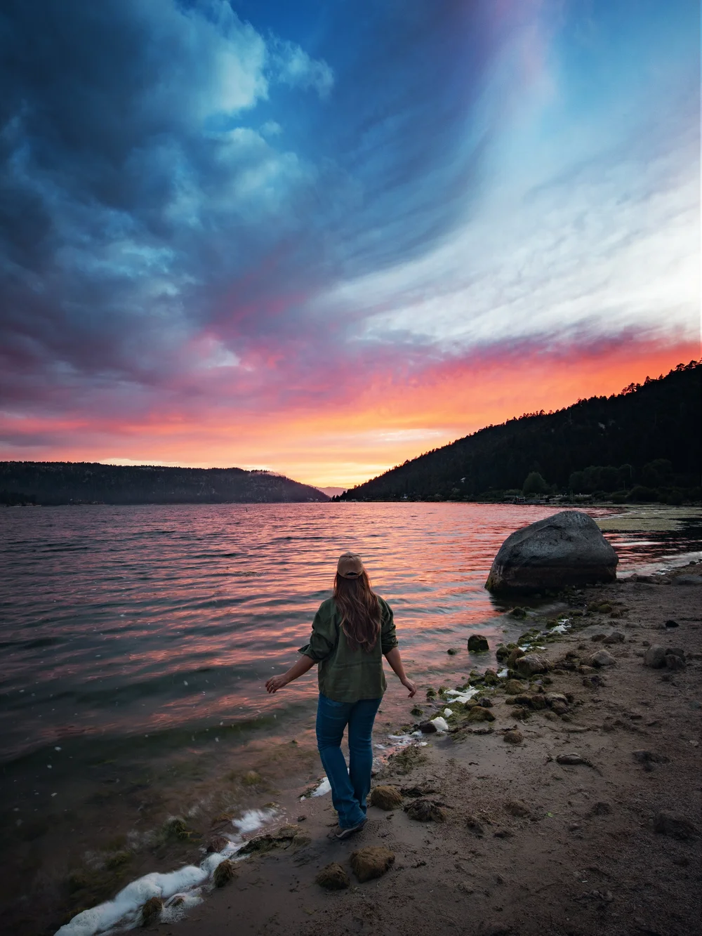 Traveler watching a vivid pink sunset from the Big Bear Lake shoreline during SkyFest, photographed by Flying Dawn Marie