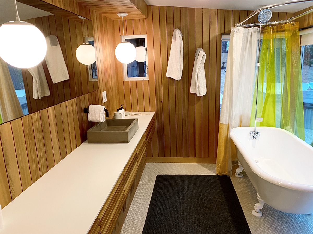 Cedar paneled cabin bathroom with white clawfoot tub and globe lighting at Colorado Lodge, Big Bear Lake